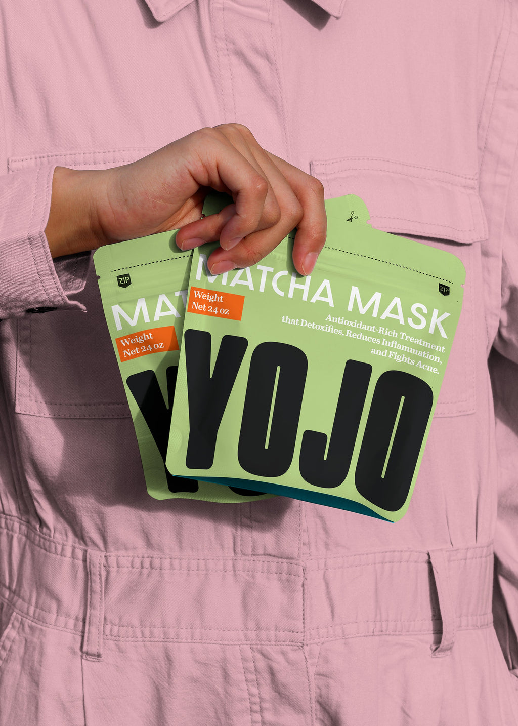 Person holding green 'YOJO' face mask packages against a pink background
