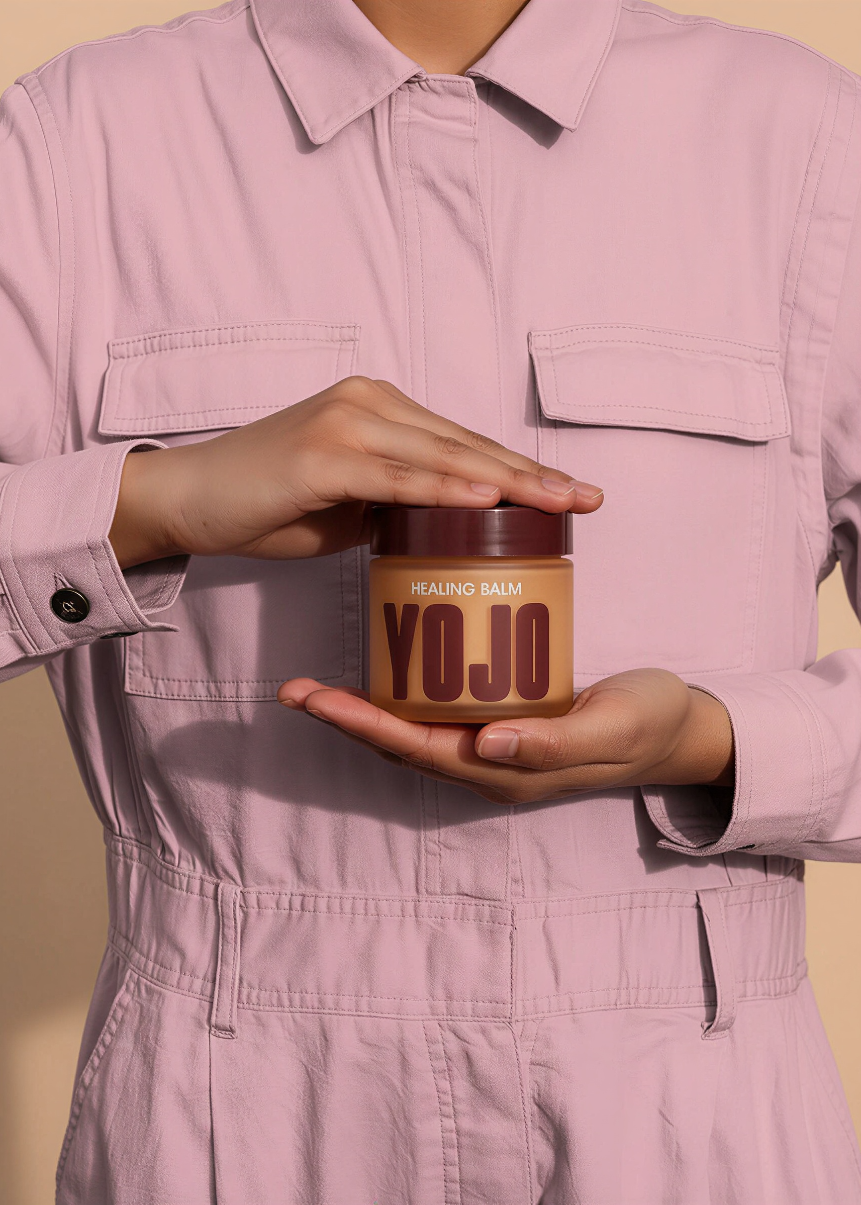Person holding a jar of 'YOJO' balm against a beige background