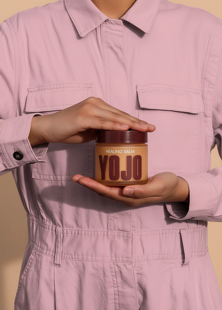 Person holding a jar of 'YOJO' balm against a beige background
